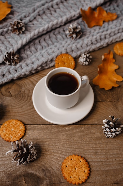 Uma xícara de café em uma mesa de madeira com biscoitos, folhas e cones