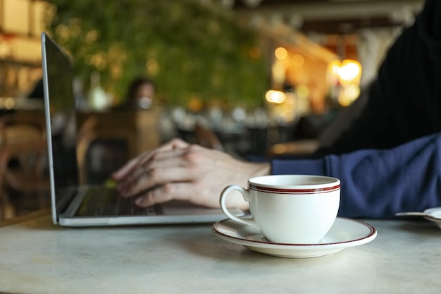 Uma xícara de café em uma mesa perto de um laptop em um café