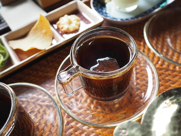 Uma xícara de café está sobre uma mesa com uma bandeja de biscoitos e um prato de biscoitos.