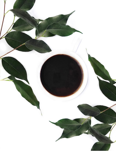 Uma xícara de café expresso preto em uma mesa branca com folhas de planta verde Bom dia conceito