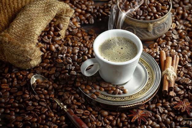 Uma xícara de café fica sobre uma pilha de grãos de café.