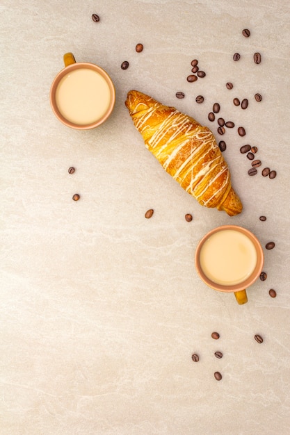 Uma xícara de café fresco com croissant. o conceito em uma superfície de pedra com grãos de café torrados, vista superior, configuração plana.