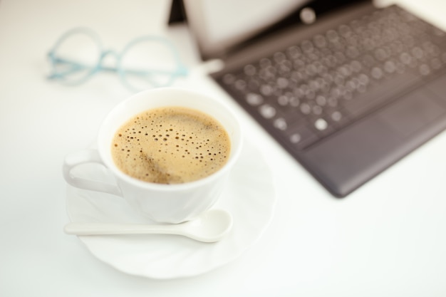 Uma xícara de café, laptop e óculos