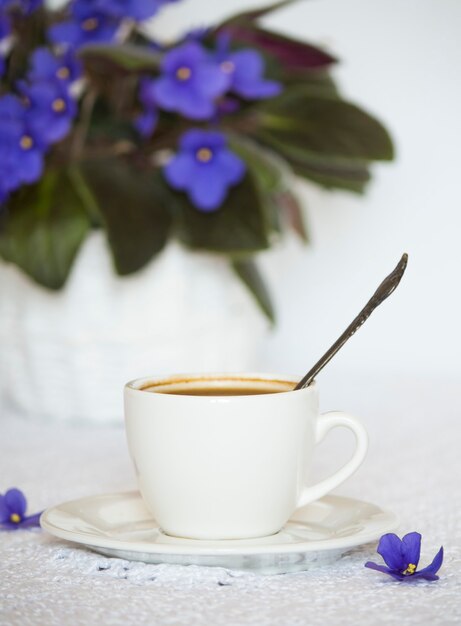 Uma xícara de café preto na mesa com uma flor de violeta caseira.