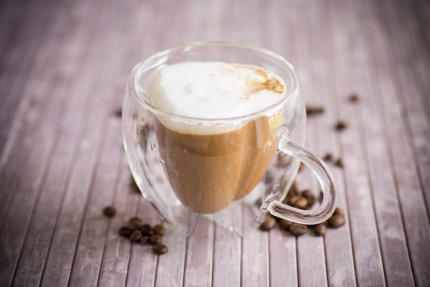 Uma xícara de café quente com leite com grãos de café em uma mesa de madeira