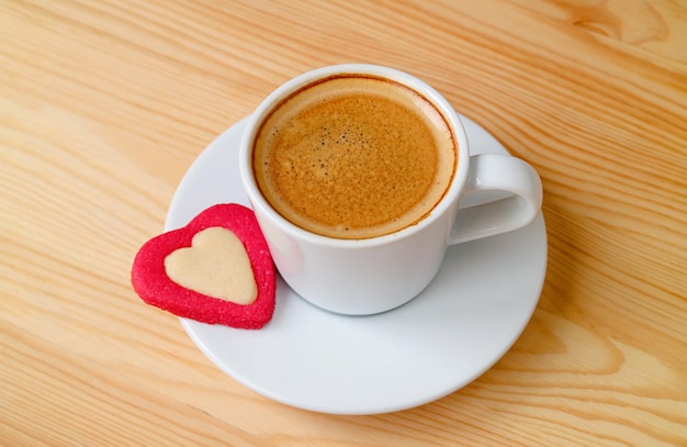 Uma xícara de café quente com um biscoito em forma de coração em fundo de madeira