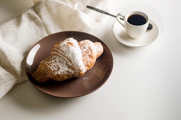 Uma xícara de café quente e croissant no prato na mesa branca