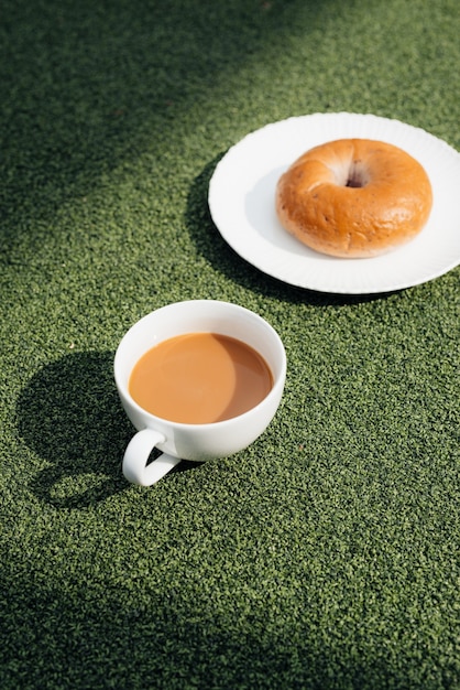 Uma xícara de café quente e donut em uma manhã fria, na grama verde com fundo de orvalho