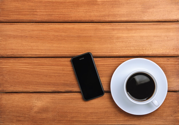 Uma xícara de café quente e telefone móvel em um fundo escuro de madeira.