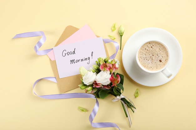 Uma xícara de café, um buquê de flores e um cartão com as palavras bom dia