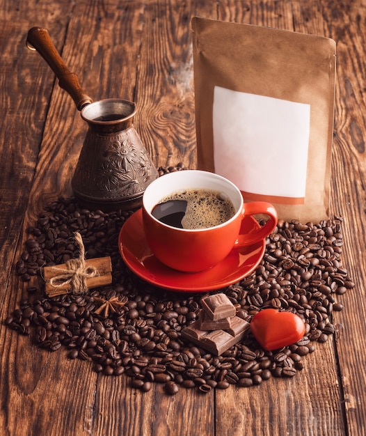 Uma xícara de café vermelha, coração, feijão, cafeteira turca e bolsa de papel artesanal em background de madeira