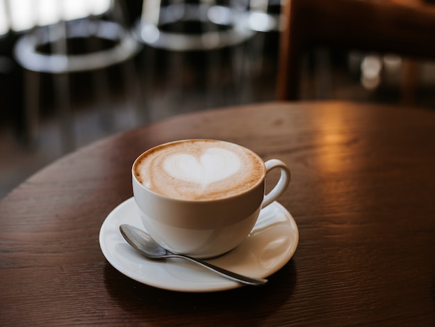 Uma xícara de cappuccino com latte art na mesa de madeira, xícara de cerâmica branca, lugar para texto. Cultura do café.