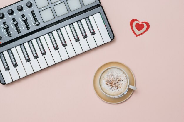 Uma xícara de cappuccino de café com canela e uma batedeira em uma superfície rosa