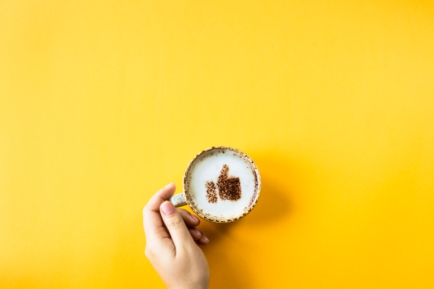 Uma xícara de cappuccino em que é desenhado um sorriso como um polegar para cima