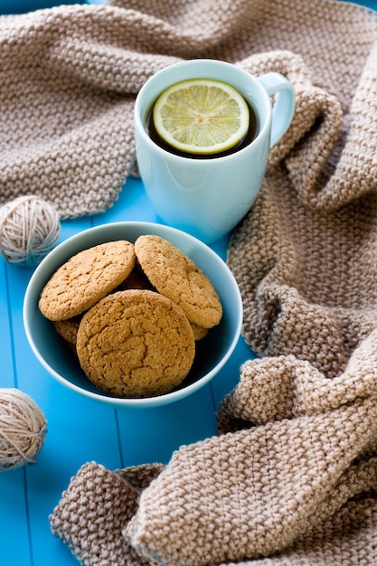 Uma xícara de chá com biscoitos de limão cobertor de malha bege está na bandeja azul