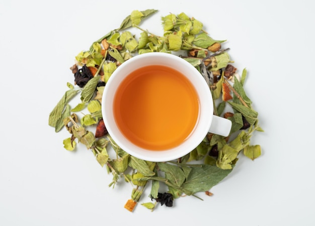 Uma xícara de chá de ervas com ervas secas espalhadas e pedaços de frutas em um fundo branco. Vista superior e copie o espaço.