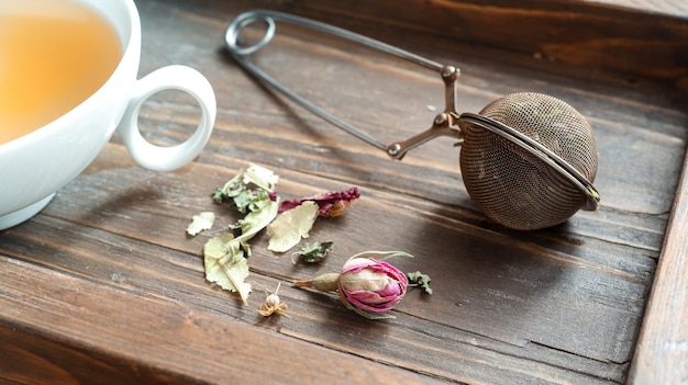 Uma xícara de chá de ervas perto da colher do infusor de chá em uma bandeja de madeira escura fechada