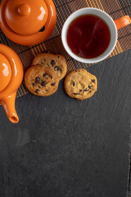 Foto uma xícara de chá e biscoitos com foto de chocolate de cima em um fundo escuro com espaço para texto