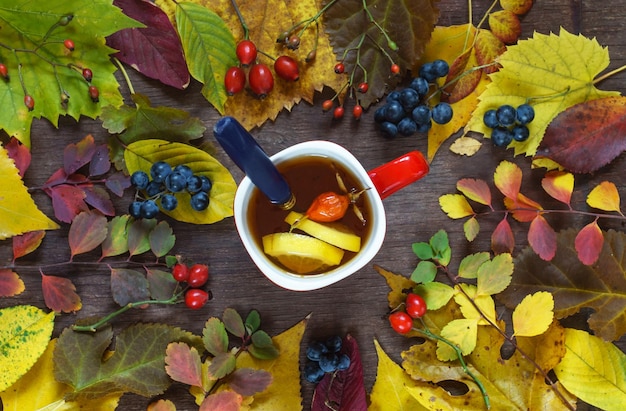 Uma xícara de chá em um fundo de folhas multicoloridas de outono e uvas em uma superfície de madeira