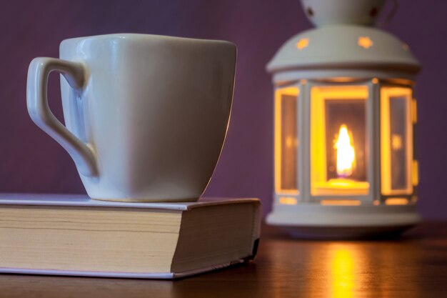 Uma xícara de chá em um livro à luz de uma lanterna com uma vela