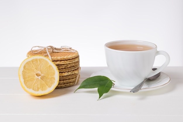 Uma xícara de chá, limão e waffles em uma mesa branca sobre um fundo claro. bolos caseiros com chá.