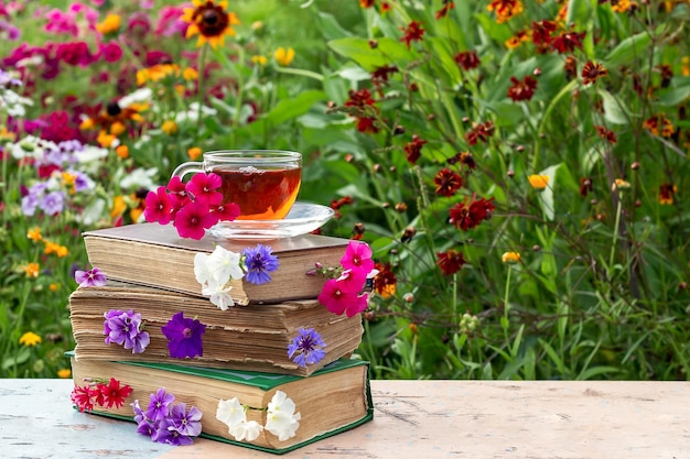 Uma xícara de chá na pilha de livros com flores dia ensolarado de verão Copiar espaço