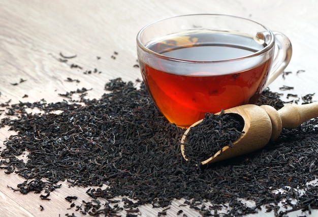 uma xícara de chá preto e folhas de chá preto secas em uma mesa de madeira