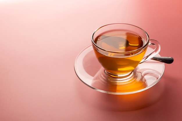 Uma xícara de chá quente acabado de fazer em um copo no fundo rosa com espaço de cópia
