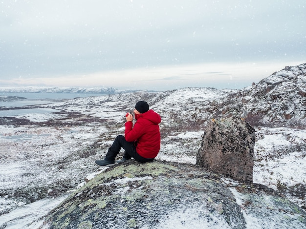 Uma xícara de chá quente nas mãos de um homem no topo de uma colina polar das colinas do norte cobertas de neve. Paisagem polar maravilhosa. O conceito de viagens.