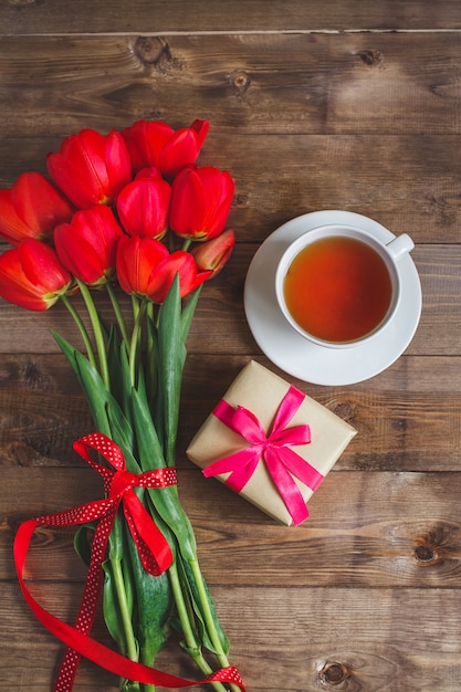 Uma xícara de chá tulipas vermelhas padrão e caixa de presente na mesa de madeira