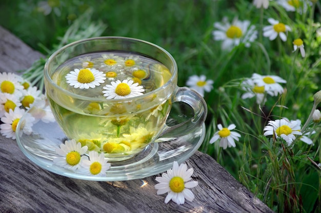 uma xícara de chá verde com margaridas em uma mesa de madeira