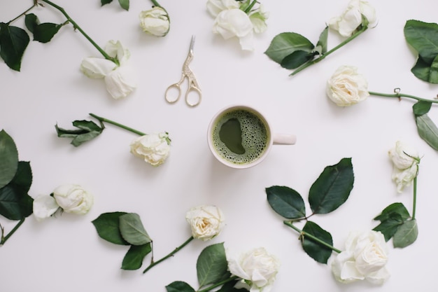 Uma xícara de chá verde com rosas brancas sobre fundo branco vista de cima