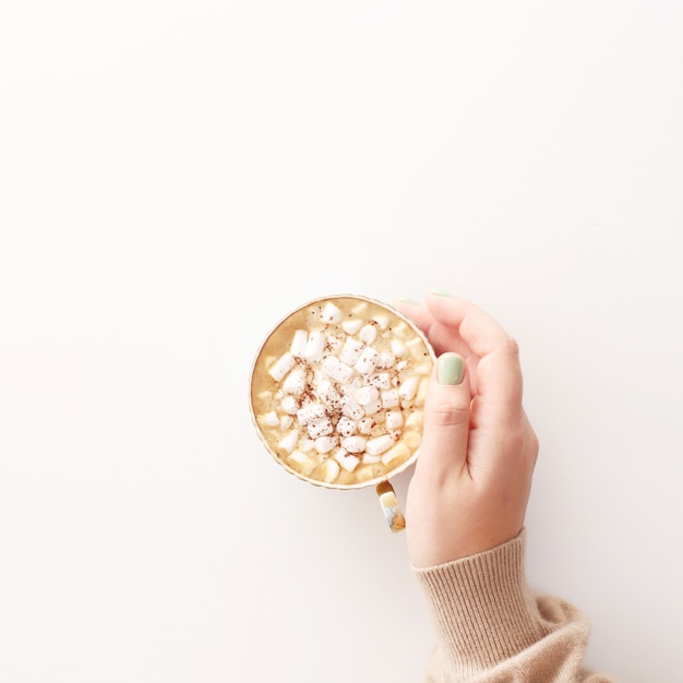 Uma xícara de chocolate com marshmallows em um fundo branco em uma mão feminina