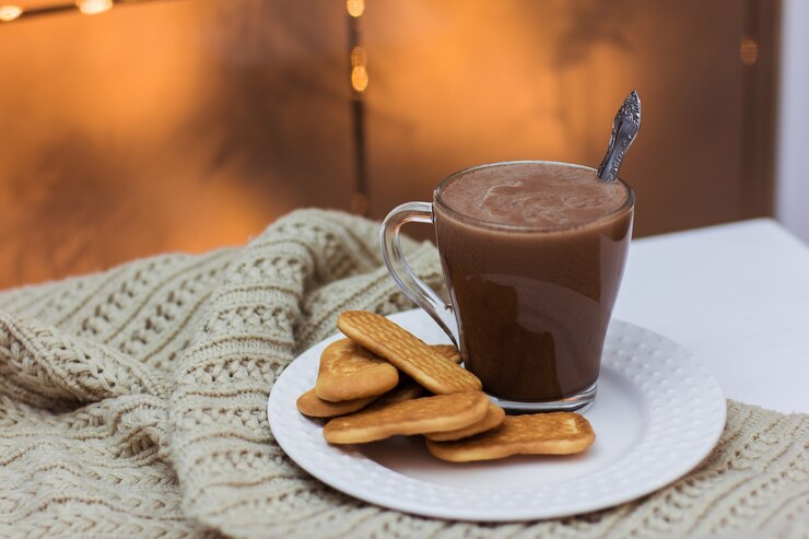 Uma xícara de chocolate e biscoitos em um prato branco sobre uma mesa branca e um lenço de malha