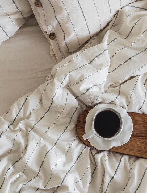 Uma xícara de expresso em uma bandeja de madeira em uma cama com roupa de cama de linho de estilo escandinavo