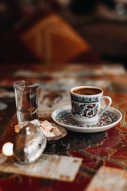 Uma xícara do tradicional café turco preto forte, delícias doces e um copinho de água. Bebidas tradicionais, conceitos de café. Vertical