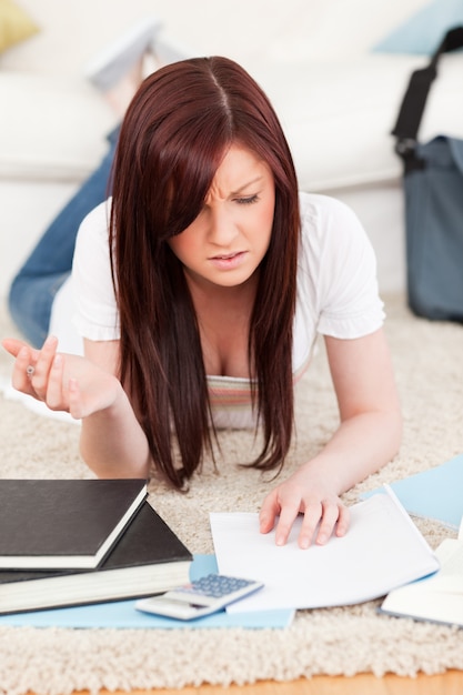 Umgekippte redhaired Frau, die für beim Lügen auf einem Teppich studiert