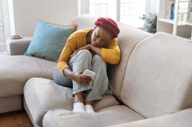 Umgekippte schwarze Frau, die auf Sofa sitzt und Telefon zu Hause benutzt