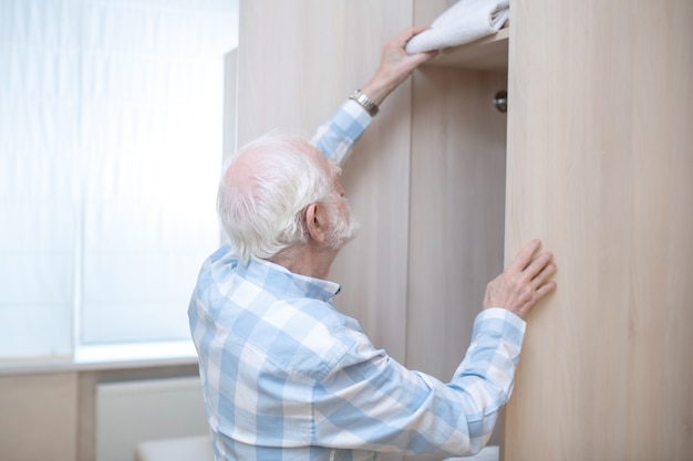 Umkleidekabine. Grauhaariger Mann in einem karierten Hemd, der einen Kleiderschrank in einer Umkleidekabine öffnet