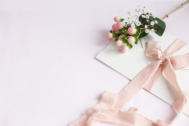 Umschlag auf weiß-rosafarbenem Hintergrund mit Pfirsichseidenband und rosa Blüten. Hochzeitseinladung. Karte zum Muttertag. Platz für Text. Platz kopieren.