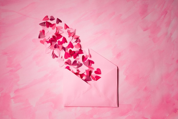 Umschlag mit Papierherzen auf rosa Hintergrund. Herzen nehmen aus offenem Umschlag heraus. Romantischer Liebesbrief.