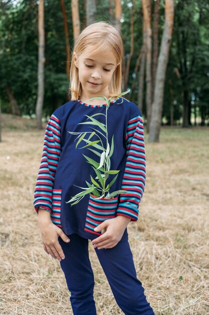 Umweltbildung für Kinder kleines Mädchen, das junge Pflanze in den Händen gegen grünen Baum hält