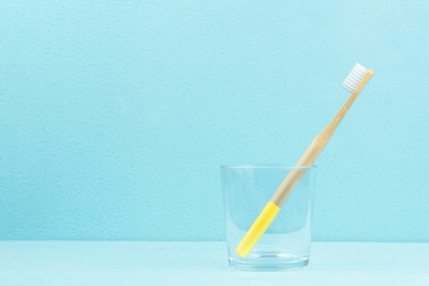 Umweltfreundliche Bambuszahnbürste in einem transparenten Glas auf einem blauen Hintergrund mit Kopienraum. Null-Abfall-Konzept.