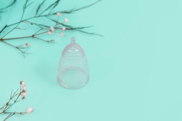 Umweltfreundliche, wiederverwendbare Menstruationstasse aus Silikon auf hellminzfarbenem Hintergrund mit kleinen Blumen und Kopierraum