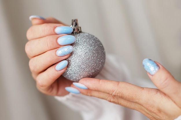 Uñas acogedoras con manicura de invierno con copos de nieve manos de mujer sosteniendo pelota de juguete de navidad