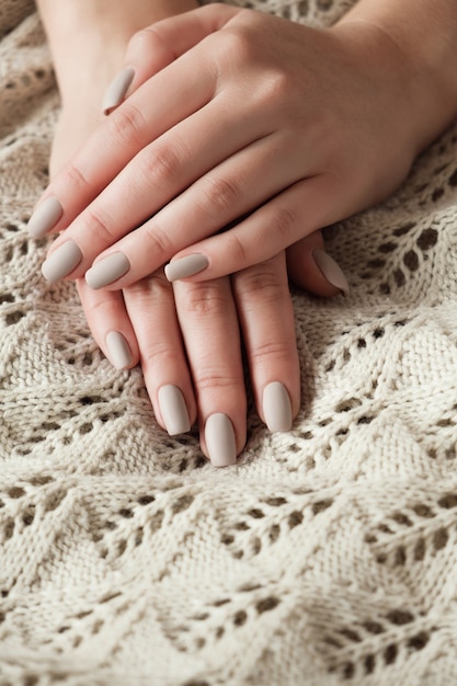 Uñas beige nude mate de cerca. Manicura de invierno u otoño, mano de mujer en suéter cálido