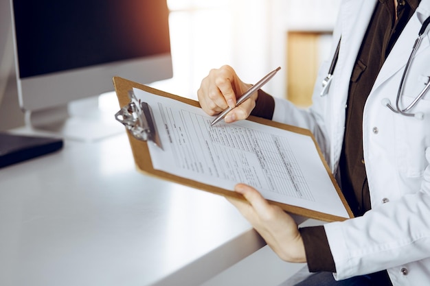 Unbekannte Ärztin benutzt Klemmbrett in sonniger Klinik. Medizinkonzept.