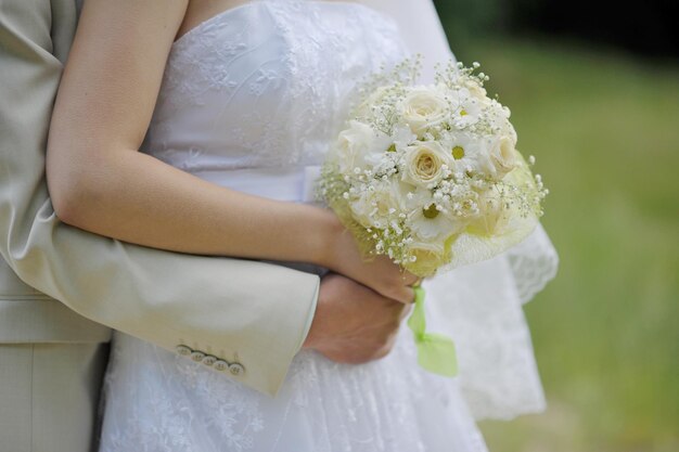 Unbekannte Braut in schönem Kleid mit Blumenstrauß und Bräutigam in weißer Jacke, die sich umarmt und im Freien posiert