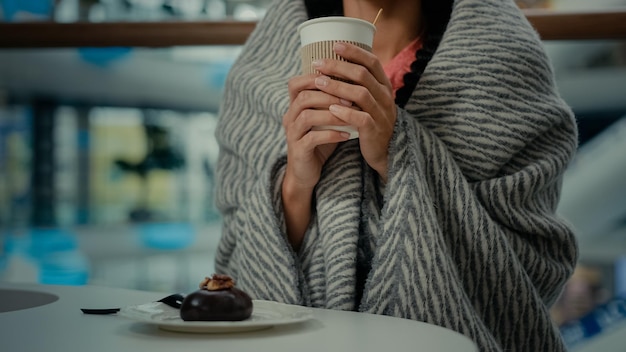 Unbekannte Frau ruht sich im Café aus und trägt eine Decke, trinkt Kaffee und genießt köstliche süße Wüste