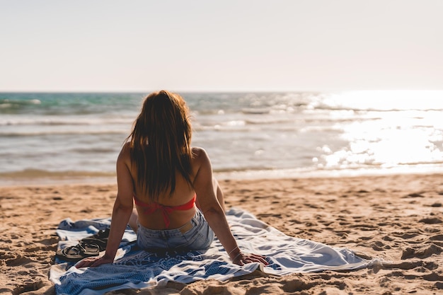 Unbekannte Frau sitzt auf einem Handtuch am Strand und beobachtet das Meer